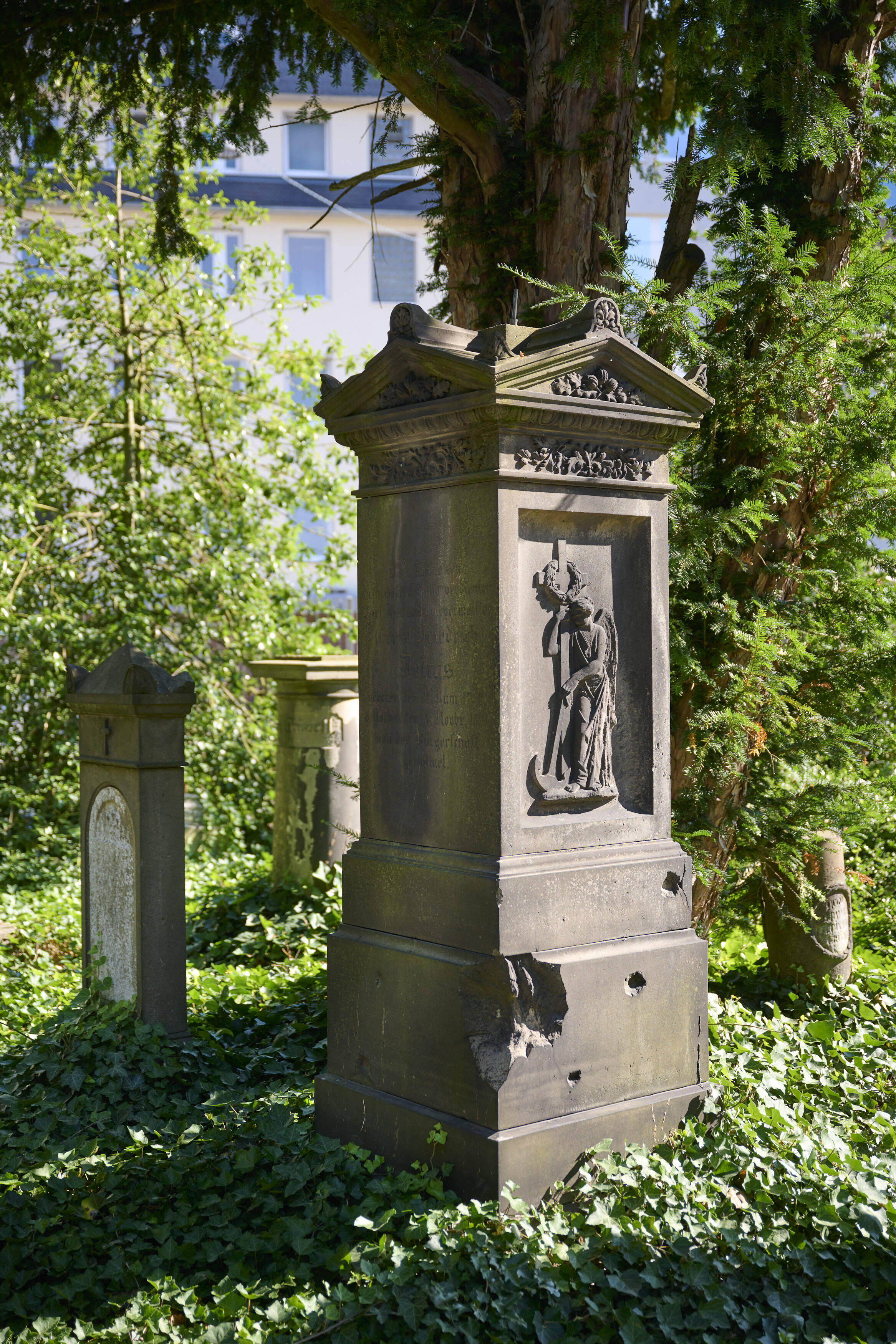 Bildtitel - Grabstätte von Ernst Friedrich Delius: Ein Grabstein mit überstehender, aufwendig verzierter Bedachung und einem erhabenen Relief einer geflügelte Frauengestalt.